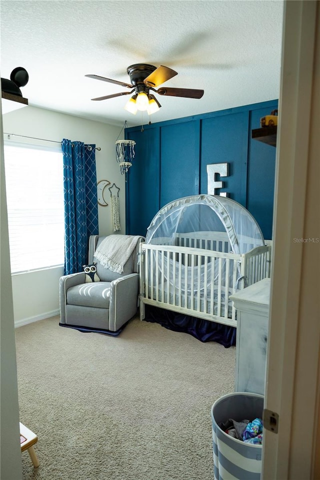 carpeted bedroom featuring ceiling fan, a textured ceiling, and a nursery area