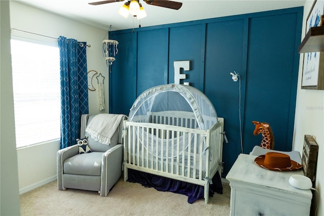 carpeted bedroom with ceiling fan and a nursery area