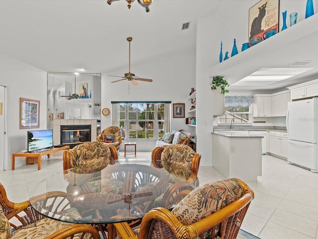 dining space featuring a tiled fireplace, a high ceiling, light tile patterned floors, and ceiling fan