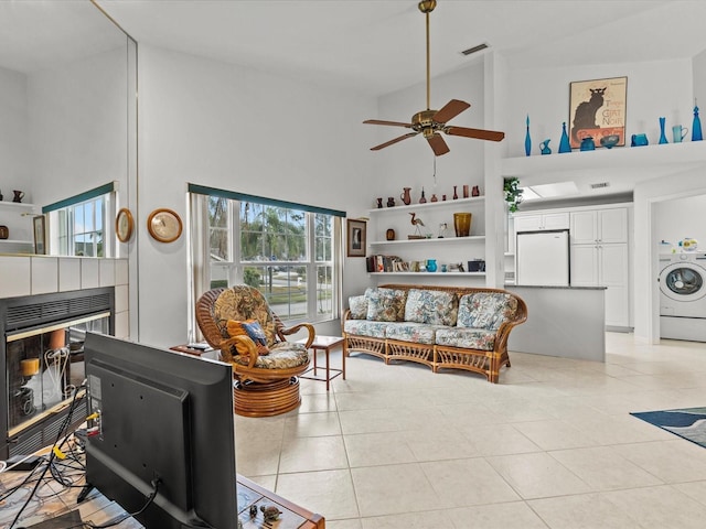 tiled living room featuring ceiling fan, a fireplace, washer / dryer, and high vaulted ceiling