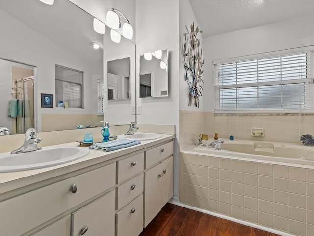 bathroom with hardwood / wood-style flooring, vanity, vaulted ceiling, and a relaxing tiled tub