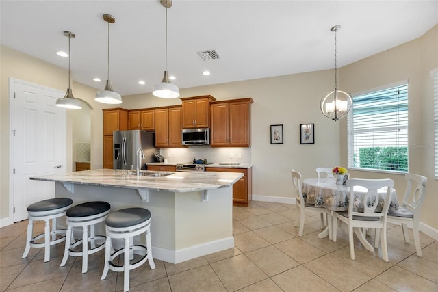 kitchen with appliances with stainless steel finishes, a spacious island, decorative light fixtures, light stone counters, and light tile patterned flooring