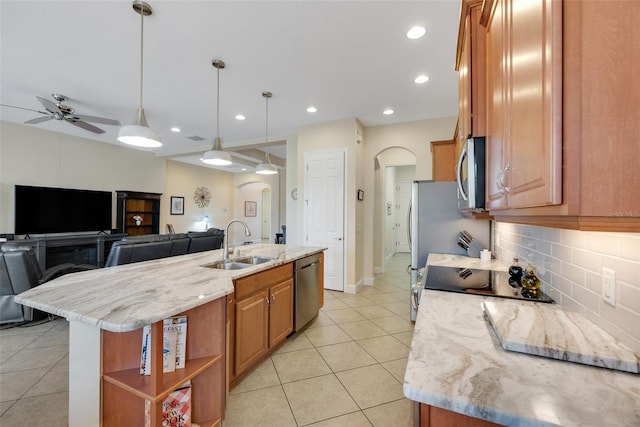 kitchen with light stone countertops, hanging light fixtures, sink, stainless steel appliances, and a center island with sink