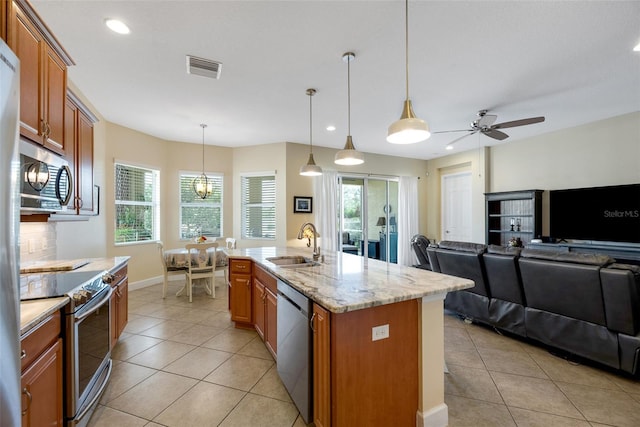 kitchen with appliances with stainless steel finishes, sink, hanging light fixtures, light stone counters, and a center island with sink