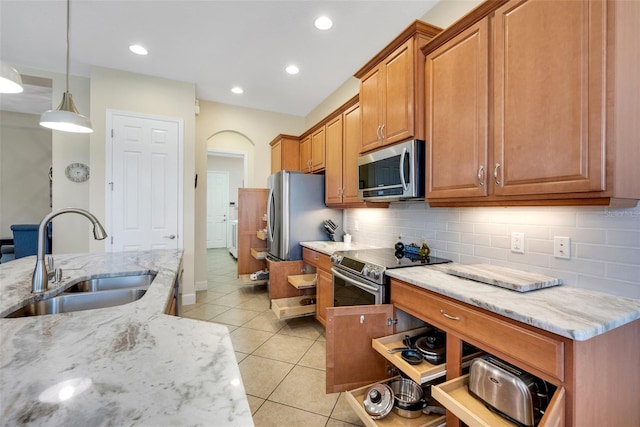 kitchen featuring pendant lighting, appliances with stainless steel finishes, sink, light stone counters, and light tile patterned floors