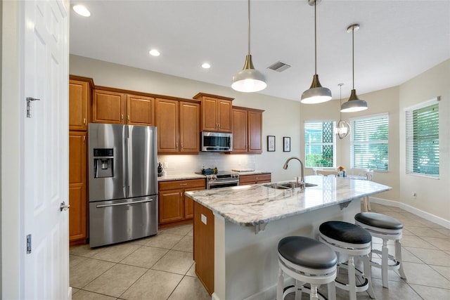 kitchen with sink, an island with sink, pendant lighting, and stainless steel appliances