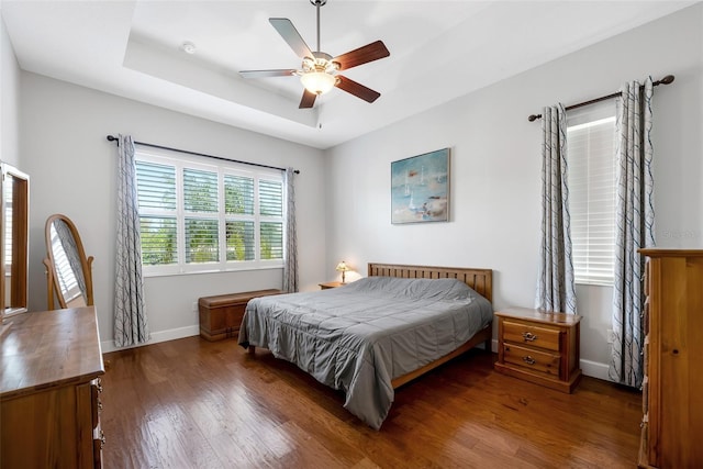 bedroom with ceiling fan, a raised ceiling, and dark wood-type flooring