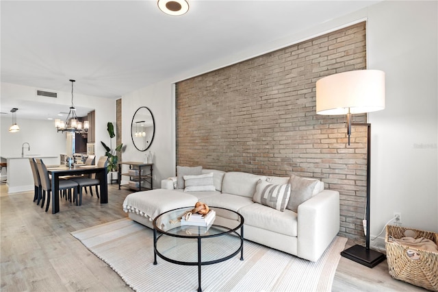 living room featuring a notable chandelier, brick wall, light hardwood / wood-style floors, and sink