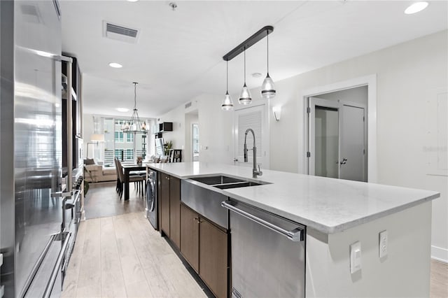 kitchen with washer / clothes dryer, sink, hanging light fixtures, a kitchen island with sink, and appliances with stainless steel finishes