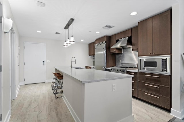 kitchen featuring sink, built in appliances, hanging light fixtures, an island with sink, and dark brown cabinets