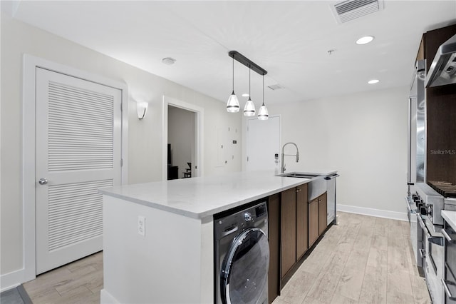 kitchen with pendant lighting, washer / dryer, a center island with sink, and light hardwood / wood-style flooring