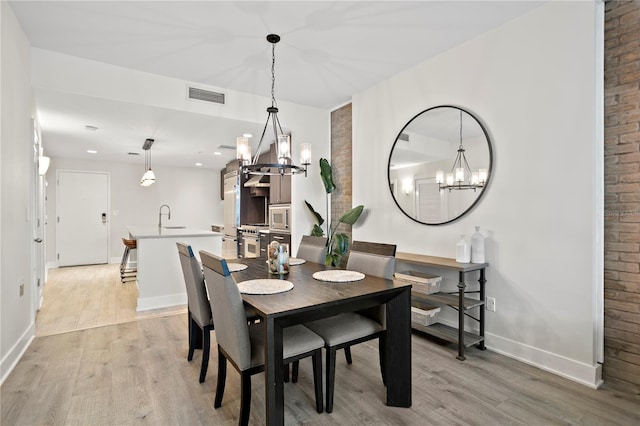 dining space with an inviting chandelier, light hardwood / wood-style floors, and sink