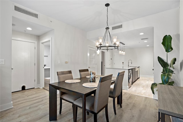 dining area with light wood-type flooring, a notable chandelier, and sink