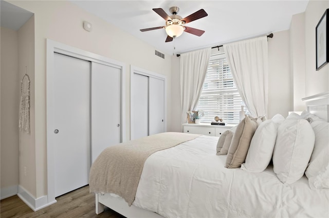 bedroom with ceiling fan, two closets, and light hardwood / wood-style flooring