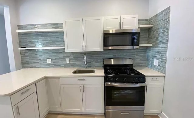 kitchen featuring backsplash, kitchen peninsula, sink, stainless steel appliances, and white cabinets