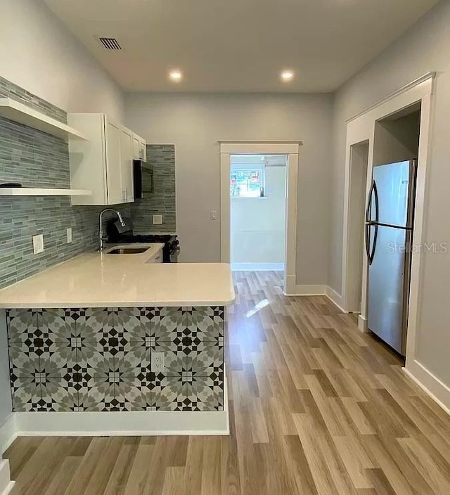 kitchen with white cabinets, tasteful backsplash, sink, kitchen peninsula, and stainless steel refrigerator