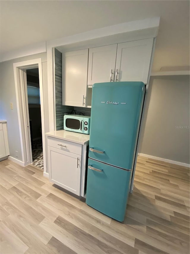 kitchen featuring backsplash, white cabinets, light wood-type flooring, and refrigerator