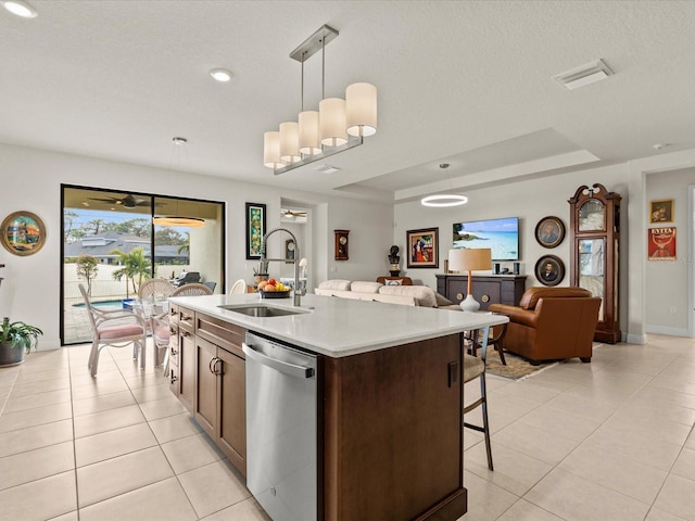 kitchen with pendant lighting, sink, dishwasher, a tray ceiling, and a center island with sink