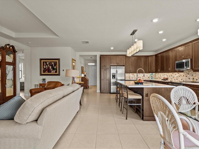 kitchen with light tile patterned floors, hanging light fixtures, stainless steel appliances, a center island with sink, and decorative backsplash