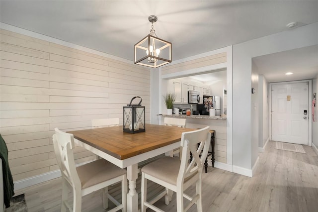 dining area featuring a chandelier, wooden walls, and light hardwood / wood-style floors