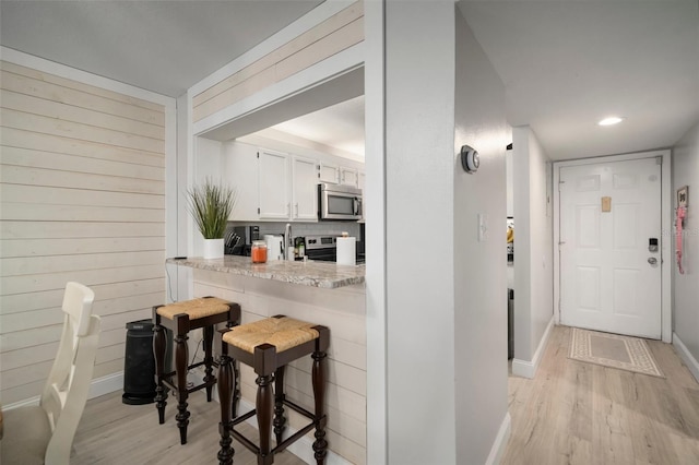 kitchen with white cabinets, light stone countertops, light hardwood / wood-style floors, decorative backsplash, and stainless steel appliances