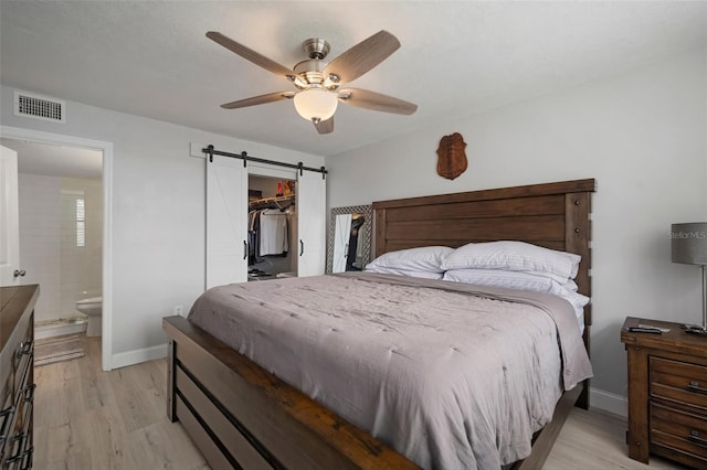 bedroom with connected bathroom, a closet, light wood-type flooring, ceiling fan, and a barn door