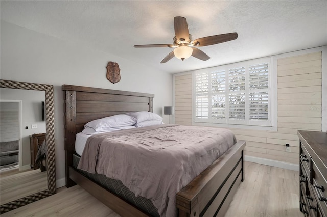 bedroom featuring ceiling fan, light hardwood / wood-style flooring, wooden walls, and a textured ceiling