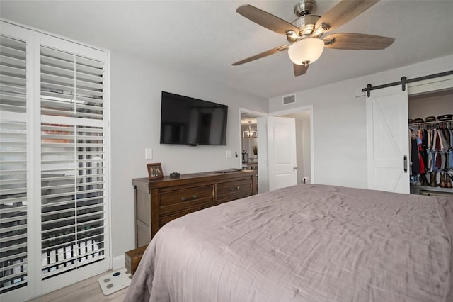 bedroom featuring wood-type flooring, a closet, ceiling fan, and a barn door