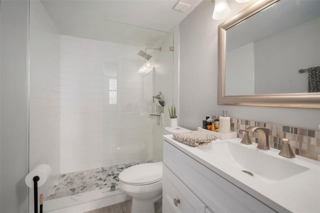 bathroom featuring backsplash, tiled shower, vanity, and toilet