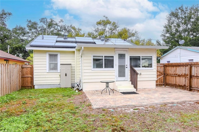 back of house featuring a yard, a patio area, and solar panels