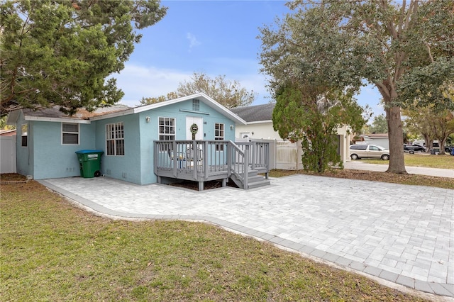 rear view of house with a wooden deck, a lawn, and a patio