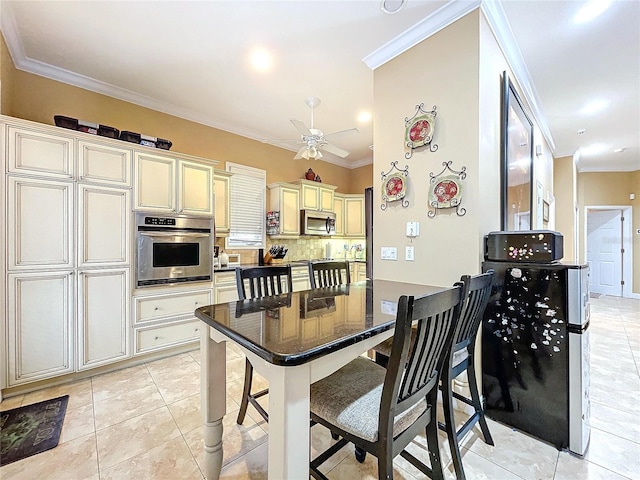 kitchen featuring cream cabinetry, appliances with stainless steel finishes, light tile patterned flooring, and crown molding