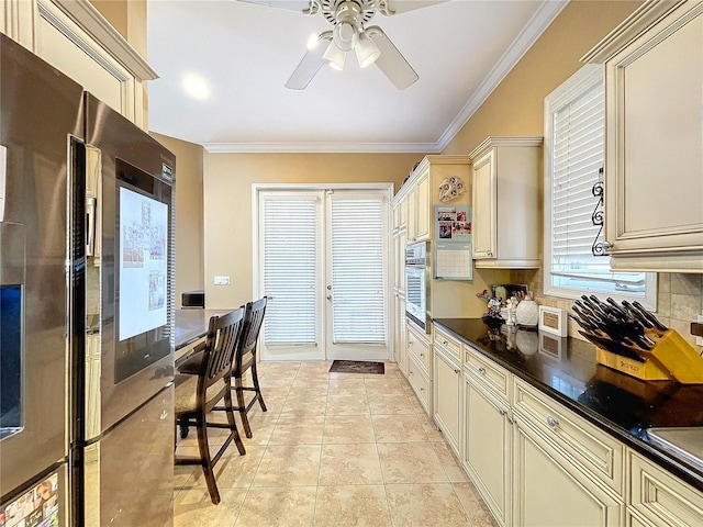 kitchen with stainless steel appliances, ornamental molding, light tile patterned floors, cream cabinetry, and french doors