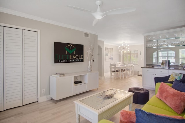 living room with ceiling fan with notable chandelier, ornamental molding, and light hardwood / wood-style floors