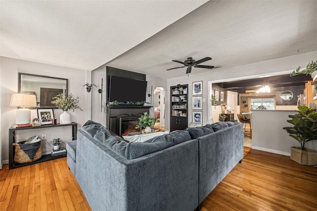 living room with a textured ceiling, ceiling fan with notable chandelier, a fireplace, and wood-type flooring