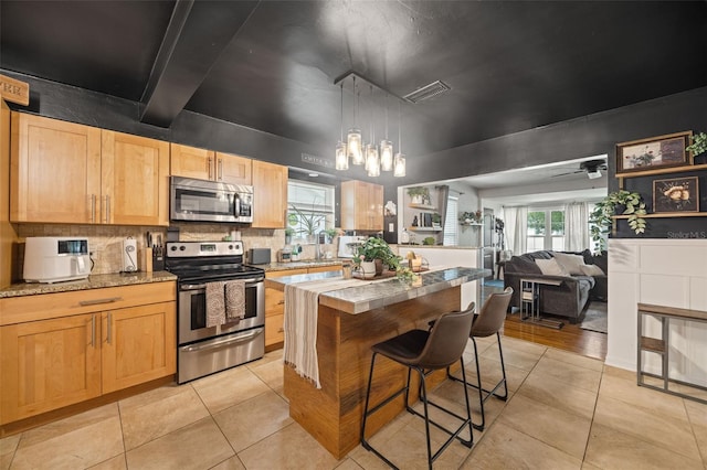 kitchen featuring ceiling fan with notable chandelier, decorative light fixtures, stainless steel appliances, a breakfast bar, and light tile patterned floors