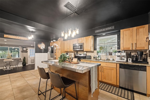 kitchen with a kitchen island, sink, light tile patterned flooring, a breakfast bar area, and stainless steel appliances