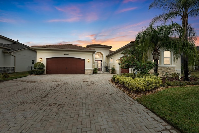 mediterranean / spanish house featuring decorative driveway, stucco siding, a gate, a garage, and stone siding