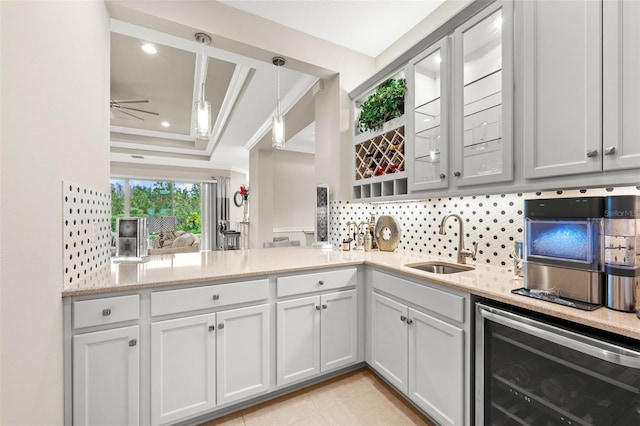 kitchen featuring wine cooler, light stone counters, a sink, tasteful backsplash, and a raised ceiling