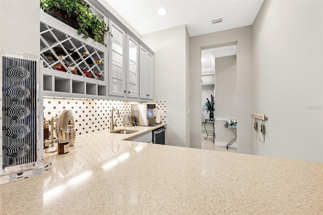 kitchen featuring tasteful backsplash, visible vents, glass insert cabinets, light stone countertops, and a sink