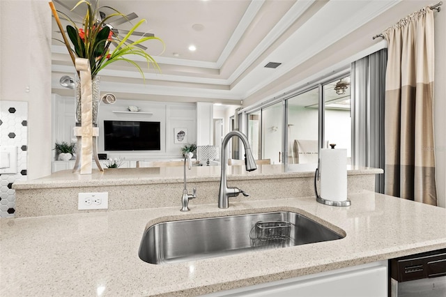 kitchen featuring a raised ceiling, stainless steel dishwasher, ornamental molding, a sink, and light stone countertops