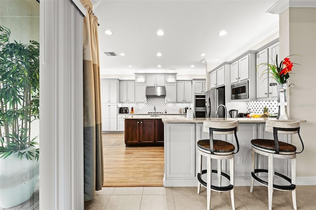 kitchen featuring visible vents, a peninsula, stainless steel appliances, under cabinet range hood, and light tile patterned flooring