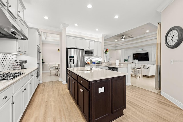 kitchen with light countertops, appliances with stainless steel finishes, open floor plan, a sink, and under cabinet range hood