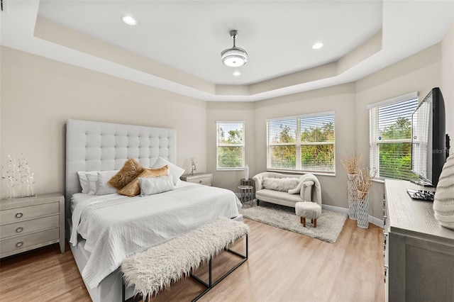 bedroom with light wood-style flooring, a tray ceiling, baseboards, and recessed lighting