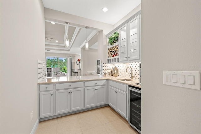 kitchen with wine cooler, a sink, light countertops, backsplash, and a raised ceiling