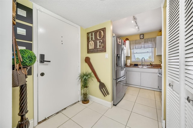 kitchen featuring white cabinetry, stainless steel refrigerator with ice dispenser, light tile patterned flooring, a textured ceiling, and sink