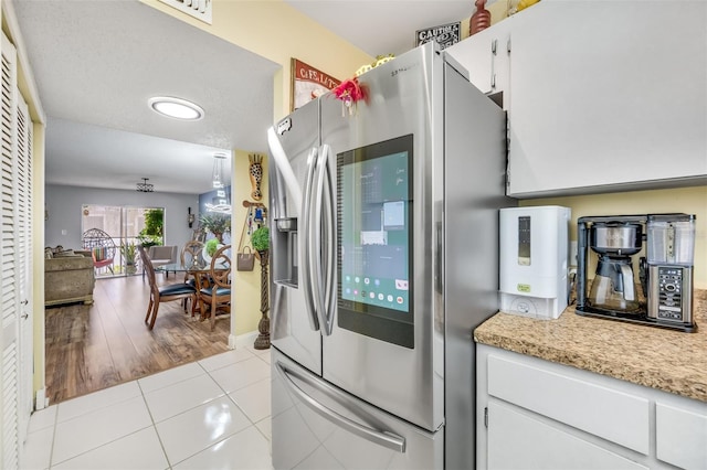 kitchen with stainless steel fridge with ice dispenser, white cabinetry, light tile patterned flooring, and light stone counters