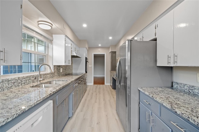 kitchen featuring sink, white cabinetry, light wood-type flooring, appliances with stainless steel finishes, and light stone countertops