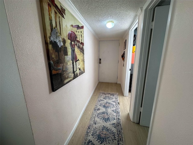 hall with a textured ceiling, ornamental molding, and light hardwood / wood-style floors