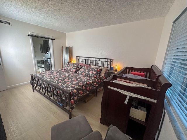 bedroom featuring a textured ceiling, light hardwood / wood-style flooring, and stacked washer and dryer